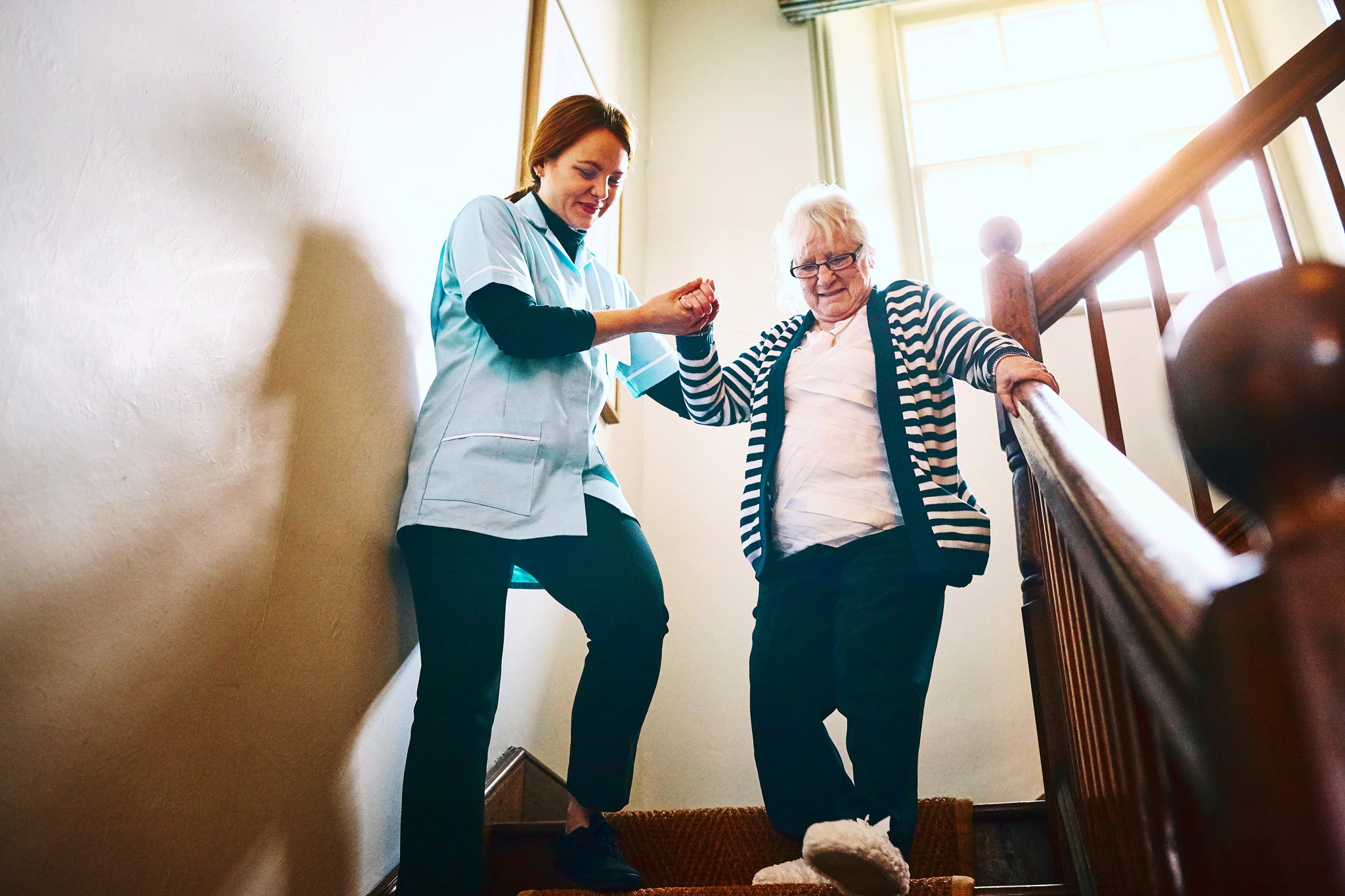 Eine Pflegerin hilft einer älteren Damen beim Treppen runterlaufen.